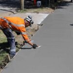 Un ouvrier en veste orange lisse du béton sur un trottoir