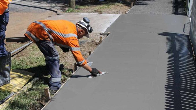 Un ouvrier en veste orange lisse du béton sur un trottoir