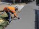 Un ouvrier en veste orange lisse du béton sur un trottoir